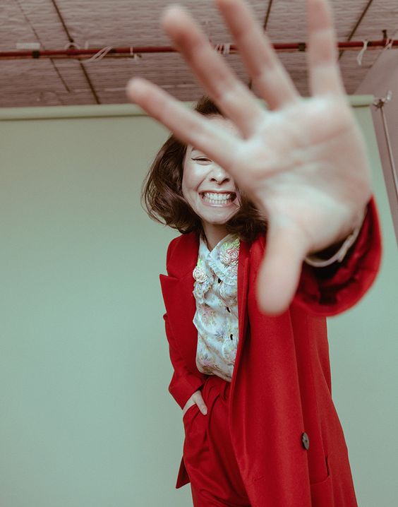 Mitski | Mitski red suit smiling and covering face | Girlfriend is Better